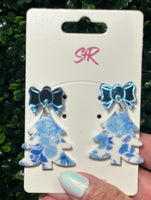 Blue floral earrings with bow details on a white card held against a green leafy background.