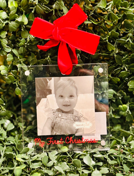 Clear photo frame with a red bow and black and white photo of a baby on green foliage.