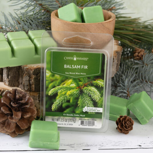 Balsam fir wax melts with packaging on a wooden surface with pine cones and branches.