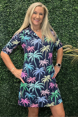 A woman modeling a short-sleeve collared dress with a colorful palm tree print on a navy background.