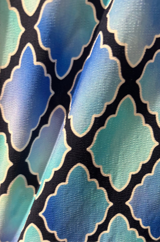 A close-up of a patterned fabric featuring a blue, teal, and light green Moroccan trellis design with navy outlines.