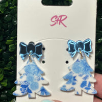 Blue floral earrings with bow details on a white card held against a green leafy background.