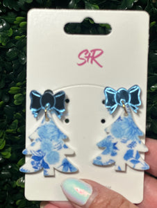 Blue floral earrings with bow details on a white card held against a green leafy background.
