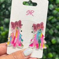 Colorful bow earrings on a white card held by a hand with a blurred green background