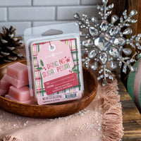 Pink wax melts in a wooden bowl with a decorative tag on a festive background