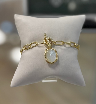 A gold link chain bracelet with a mother of pearl charm