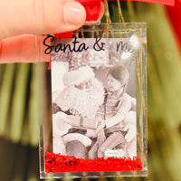 Glitter Acrylic Photo Ornament - Santa & Me 
Capture a memory and sparkle all season long with our Acrylic Glitter-Filled Photo Ornament! Designed to hold a wallet-size photo, this clear acrylic ornament is filled with festive glitter that adds the perfect holiday shimmer. A thoughtful keepsake for your own tree or a heartfelt gift for someone special.

