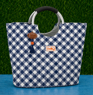 Loopi Tote Bag - Gameday Gingham Navy + Orange
Fit &amp; Details | Spacious tote silhouette with structured base
Handles | Sleek silver ring handles with a cushioned grip for comfortable carrying
Exterior | Durable, wipe-clean fabric in a classic navy gingham print
Accents | Coordinating navy tassel and football charm zipper pull
Branding | Signature Swig patch on front