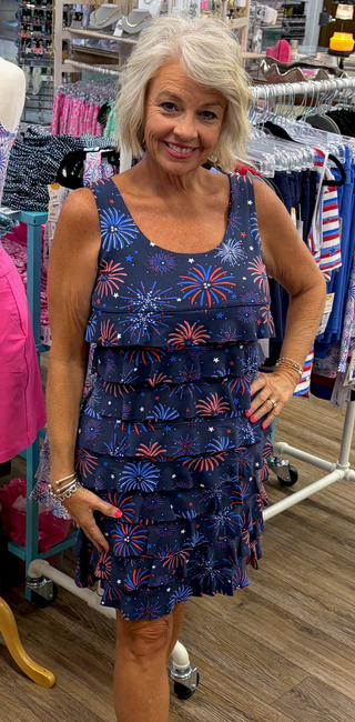 Lulu-B Cha Cha sleeveless dress with scoop neckline, front and back ruffle details, straight hemline, flattering fit, lightweight comfortable dress for travel, vacations, resort wear, and everyday style.
Printed on a navy blue dress with firework detail print