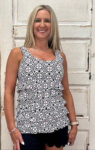 The Lulu-B Cha Cha Tank in the DGBW print features a sophisticated floral pattern in black, tan, and white with a bright hot pink center in each bloom — front and back ruffles and a scoop neckline add a flirty, elevated finish to a print that balances classic neutrals with a bold, unexpected pop of color.