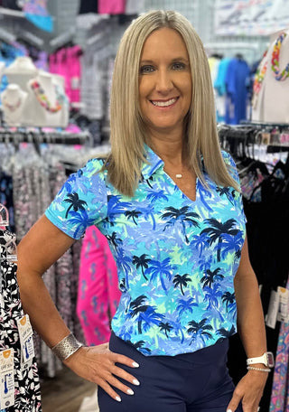 The Lulu-B V-Neck Short Sleeve Collar Top in the PTBL print features a serene blue palm tree pattern — butter-soft, wrinkle-free fabric, a polished collar detail, V-neckline, and UPF 50+ protection give it an elevated, resort-inspired look that transitions effortlessly from brunch to sightseeing to a dressed-up evening out. Lightweight and breathable, it packs without creasing so you always step out looking fresh, no matter where the day takes you.