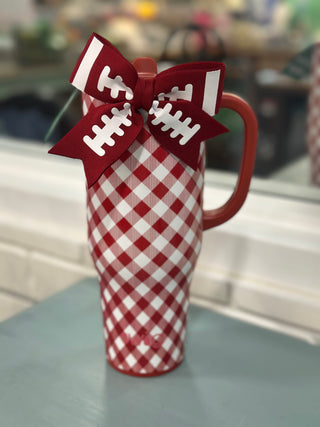 A red and white gingham patterned tumbler with a red handle, decorated with a red and white football-themed ribbon bow on top