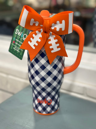 A Swig brand insulated travel mug with a navy and white gingham pattern, an orange handle, and an orange football-shaped ribbon bow with white laces on top.