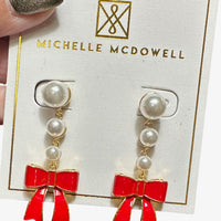 Pearl earrings with red bows on a Michelle McDowell branded card.