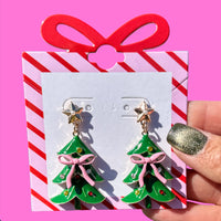 Add a festive touch to your holiday look with the Pink Bow Christmas Tree Earrings. These charming post-back earrings measure 2" tall x 1" wide, featuring a playful pink bow atop a classic Christmas tree design. Lightweight and cheerful, they’re perfect for celebrating the season in style.