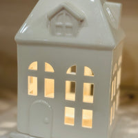 Charming porcelain house fragrance warmer with glowing windows. Perfect for farmhouse or rustic decor. Safely warms wax melts for cozy scent and ambiance.
