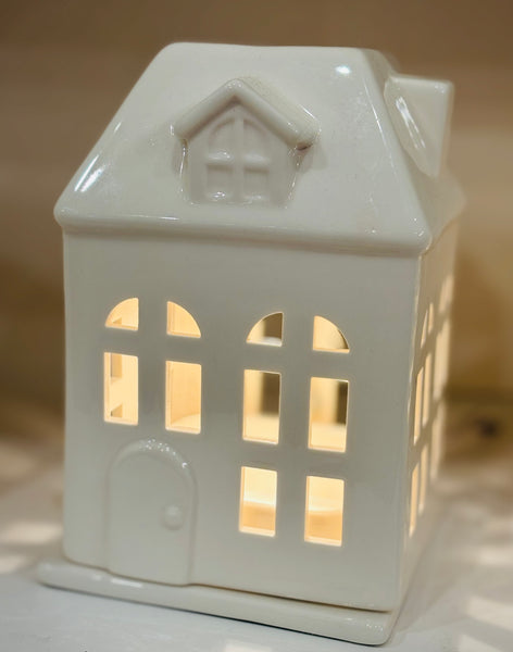 Charming porcelain house fragrance warmer with glowing windows. Perfect for farmhouse or rustic decor. Safely warms wax melts for cozy scent and ambiance.