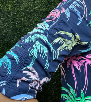 Close-up of a person wearing dark navy tropical print dress with a gathered elastic cuff, featuring palm tree patterns in bright pink, teal, green, and white