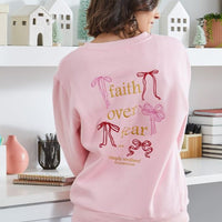 Person wearing a pink sweatshirt with 'faith over fear' text in a home setting