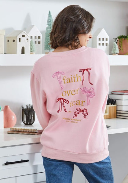 Person wearing a pink sweatshirt with 'faith over fear' text in a home setting