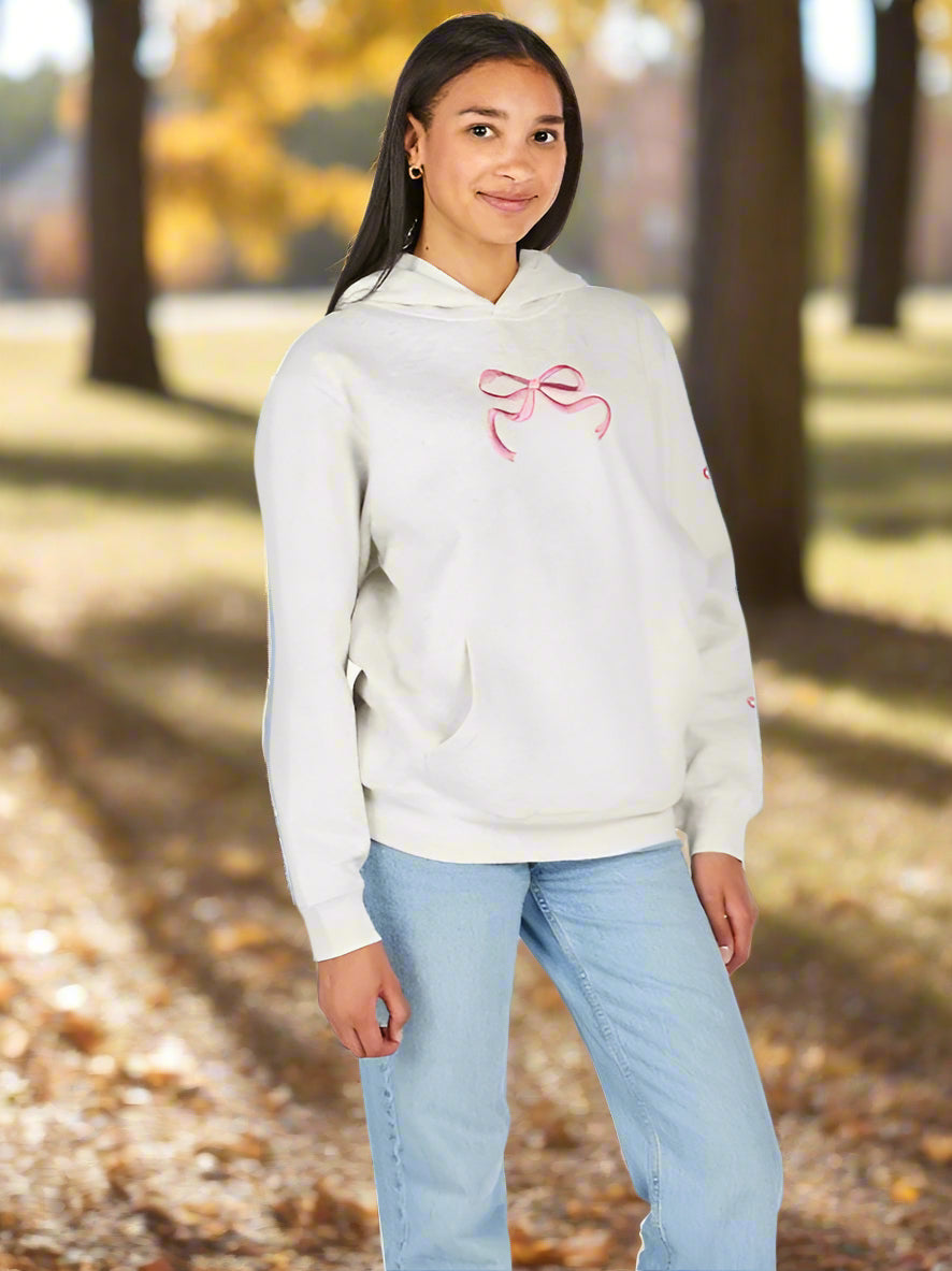 Person wearing a light gray hoodie with a pink bow design and light blue jeans on a white background