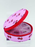 Pink pill organizer with cherry design on a white background
