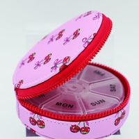 Pink pill organizer with cherry design on a white background