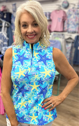 The Sleeveless Zip Top in the Starfish print features a vibrant turquoise base with yellow and blue starfish details and a quarter-zip neckline that makes it as easy to style as it is to wear — lightweight, cooling fabric and UPF 50 protection make it the perfect top for active days, outdoor adventures, or casual warm-weather outings.