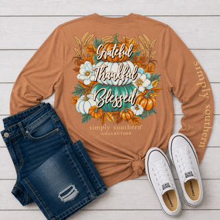 A flat-lay of a rust-orange long-sleeve graphic shirt with autumn-themed text and illustration, The shirt features 'Grateful Thanksgiving Blessed' with pumpkins, flowers, and wheat, and 'simply southern' is printed down one sleeve.