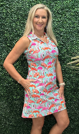 A woman modeling a sleeveless collared mini dress with a colorful flamingo print on a light blue background.