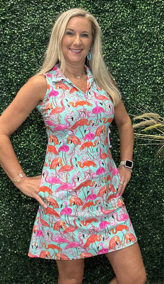 A woman modeling a sleeveless collared mini dress with a colorful flamingo print on a light aqua background